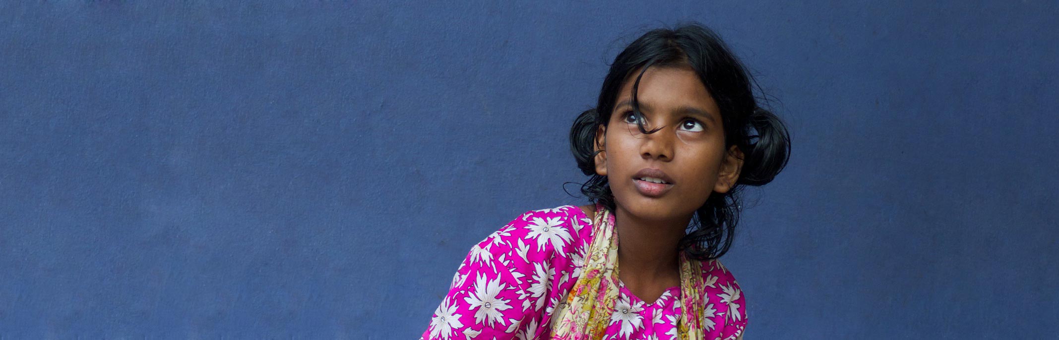 fille indienne devant un mur bleu, regardant vers le ciel